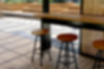 Wooden stools at a high table in a sunlit outdoor space. Wooden planters as outdoor seating area promoting sustainability with wood.