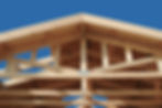 Wooden roof trusses under a clear blue sky. The structure features solid timber beams with construction markings